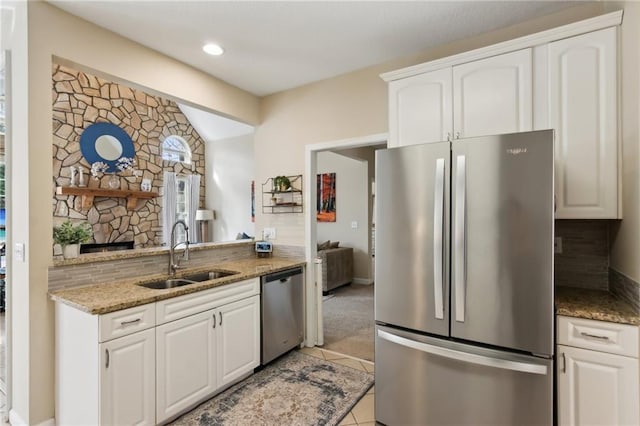 kitchen with light tile patterned floors, stainless steel appliances, white cabinetry, a sink, and light stone countertops