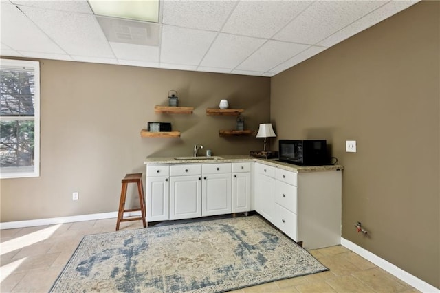 kitchen with a paneled ceiling, black microwave, white cabinetry, and a sink