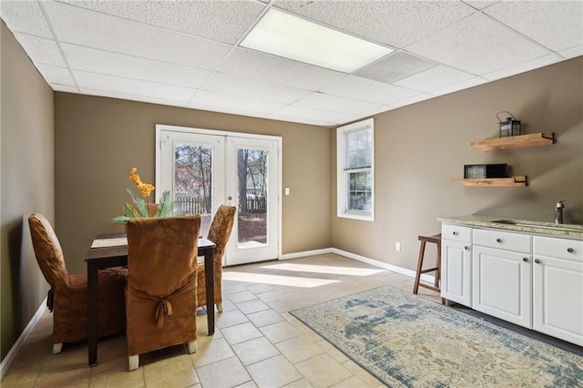 dining space featuring light tile patterned floors, french doors, a drop ceiling, and baseboards