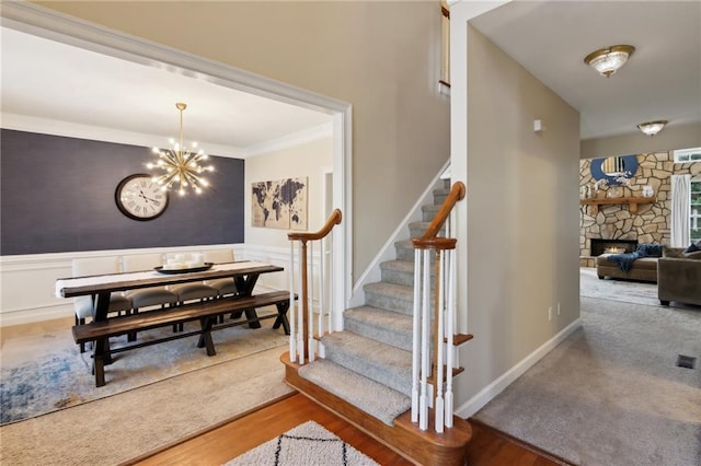 stairs featuring a wainscoted wall, a stone fireplace, wood finished floors, and a notable chandelier