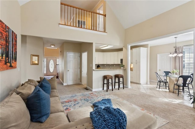 living room with an inviting chandelier, baseboards, high vaulted ceiling, and light colored carpet