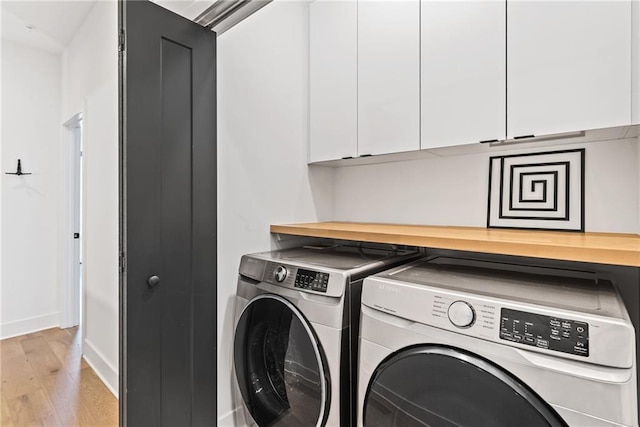 washroom with cabinet space, light wood-style flooring, separate washer and dryer, and baseboards