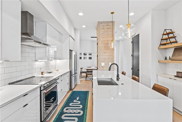 kitchen featuring white cabinetry, high end appliances, modern cabinets, wall chimney exhaust hood, and a sink