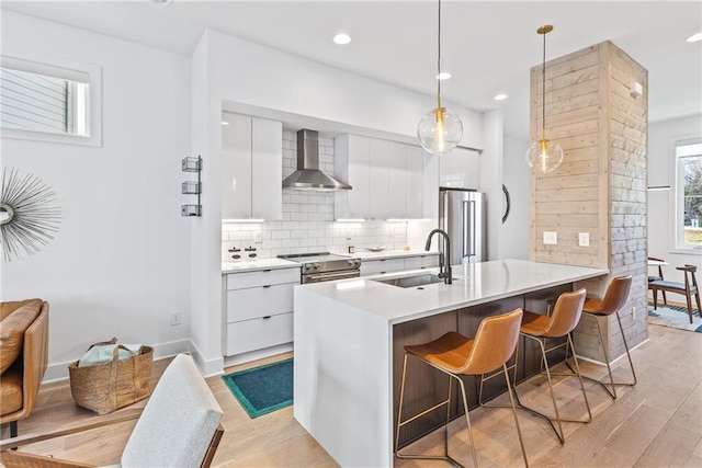 kitchen with modern cabinets, tasteful backsplash, wall chimney range hood, appliances with stainless steel finishes, and a sink