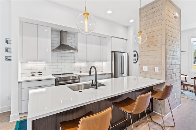 kitchen featuring light wood-type flooring, modern cabinets, wall chimney exhaust hood, premium appliances, and a sink