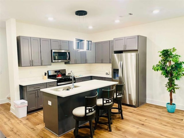 kitchen featuring a breakfast bar area, stainless steel appliances, light wood-style floors, light countertops, and an island with sink