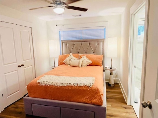 bedroom with a ceiling fan, visible vents, baseboards, and wood finished floors