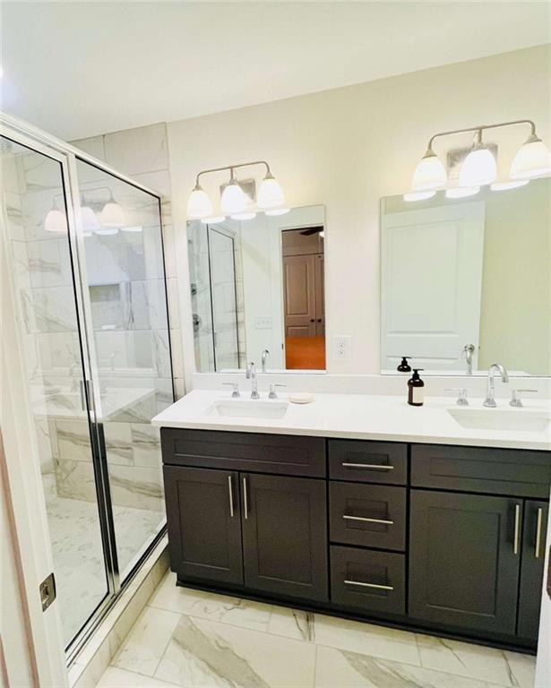 full bathroom with marble finish floor, a sink, a shower stall, and double vanity