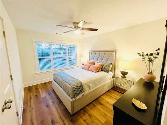 bedroom with a ceiling fan, visible vents, baseboards, and wood finished floors