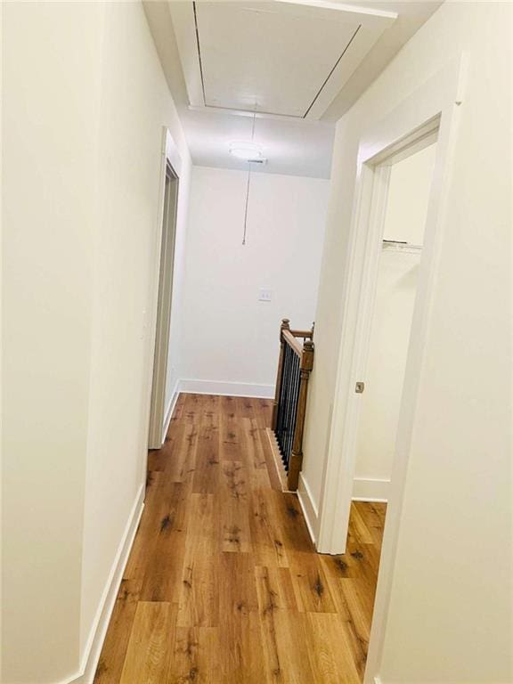 hallway featuring attic access, baseboards, and light wood finished floors