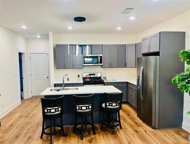 kitchen with a kitchen island with sink, appliances with stainless steel finishes, light countertops, and a breakfast bar area