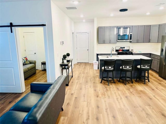 kitchen with pendant lighting, light countertops, a barn door, appliances with stainless steel finishes, and an island with sink