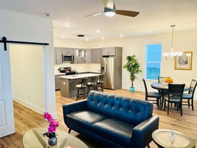 living room featuring light wood finished floors, a barn door, baseboards, ceiling fan with notable chandelier, and recessed lighting