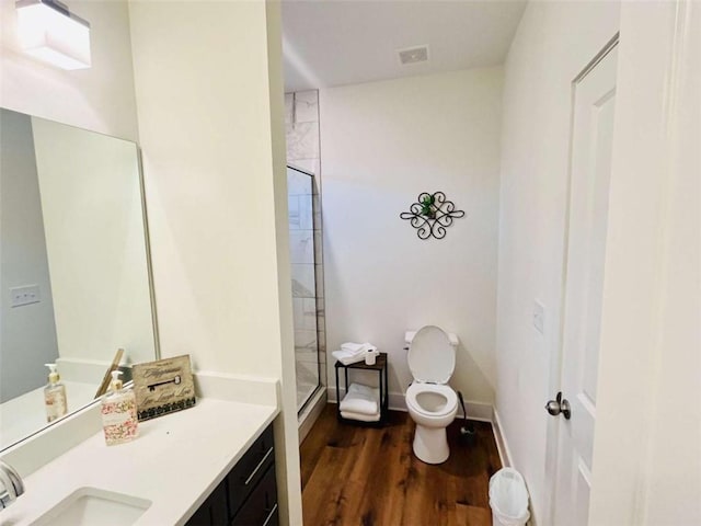 full bath featuring toilet, a tile shower, vanity, wood finished floors, and baseboards