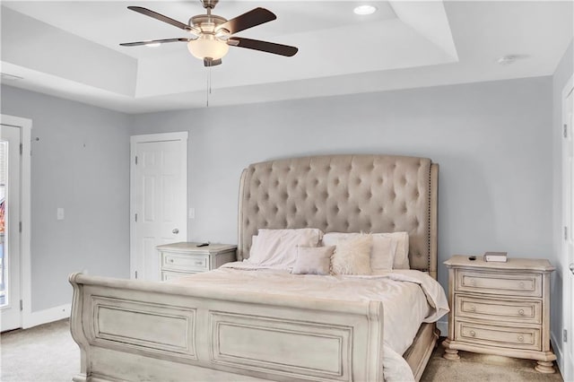 carpeted bedroom with a raised ceiling and ceiling fan