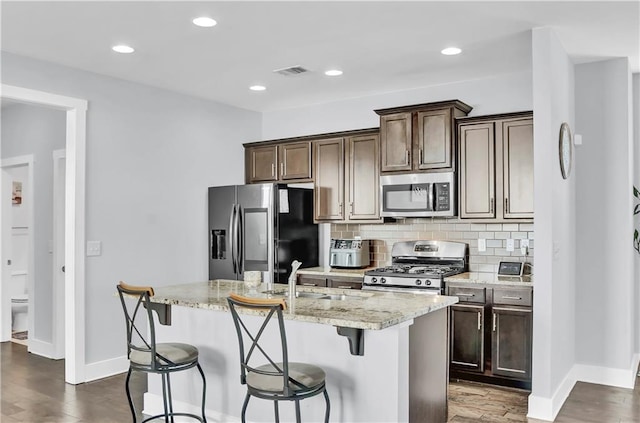 kitchen featuring sink, dark wood-type flooring, light stone counters, a center island with sink, and appliances with stainless steel finishes