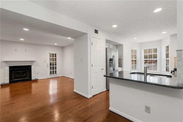 kitchen with stainless steel refrigerator with ice dispenser, sink, a textured ceiling, kitchen peninsula, and hardwood / wood-style floors