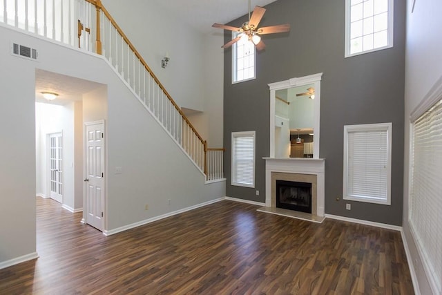 unfurnished living room with a wealth of natural light, dark wood-type flooring, and ceiling fan