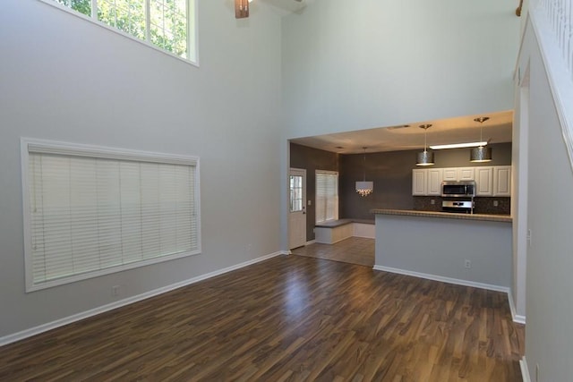 unfurnished living room with a high ceiling, dark hardwood / wood-style floors, and ceiling fan