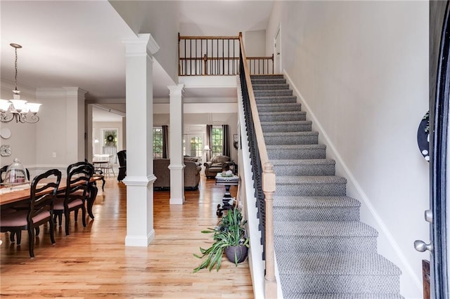 staircase featuring decorative columns, ornamental molding, hardwood / wood-style floors, and a chandelier