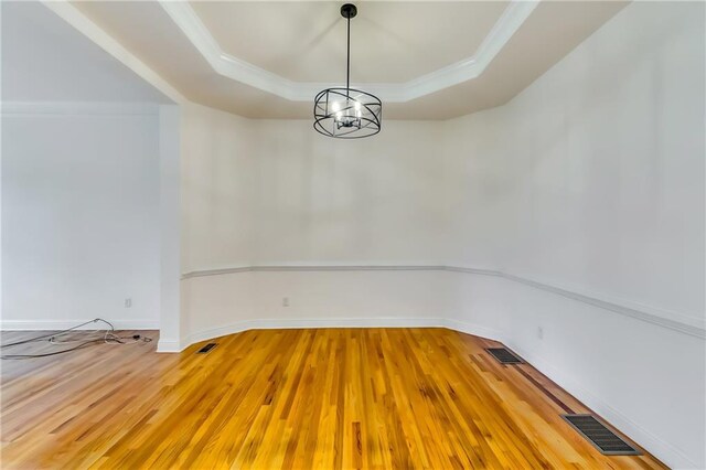 spare room with an inviting chandelier, wood-type flooring, a tray ceiling, and ornamental molding