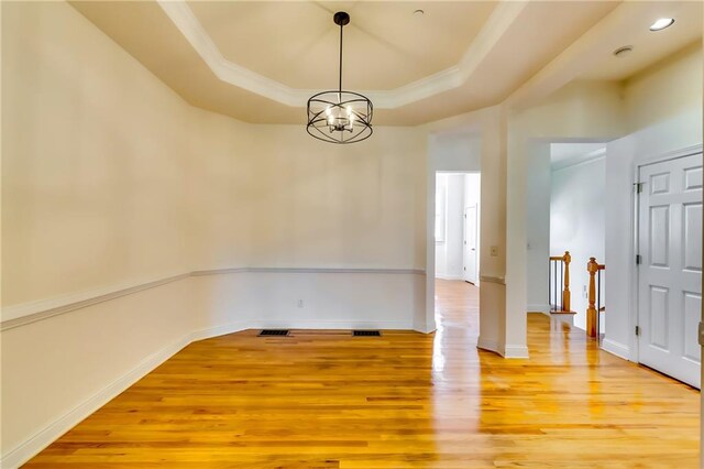 spare room featuring a raised ceiling, light hardwood / wood-style floors, and an inviting chandelier