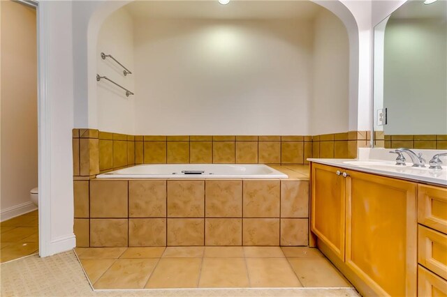 bathroom featuring a relaxing tiled tub, vanity, tile patterned flooring, and toilet