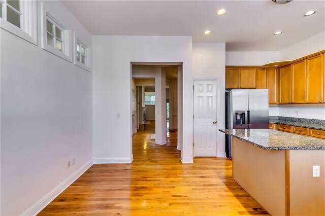 kitchen with dark stone counters, stainless steel refrigerator with ice dispenser, a center island, and light hardwood / wood-style flooring