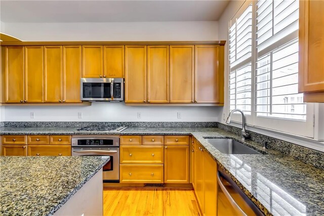 kitchen with dark stone countertops, appliances with stainless steel finishes, sink, and light hardwood / wood-style flooring