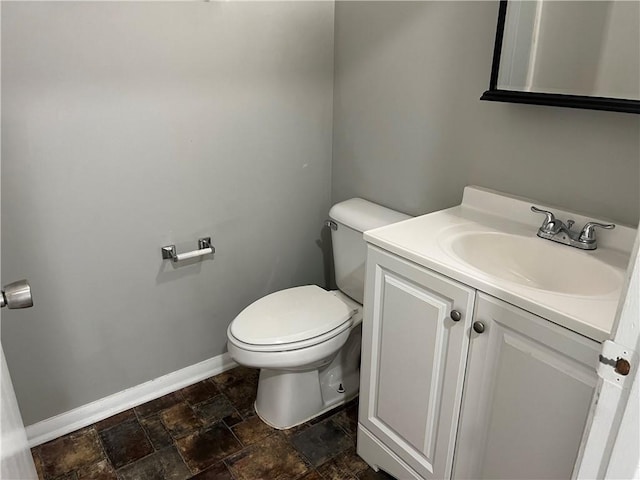 half bathroom with stone finish floors, toilet, vanity, and baseboards