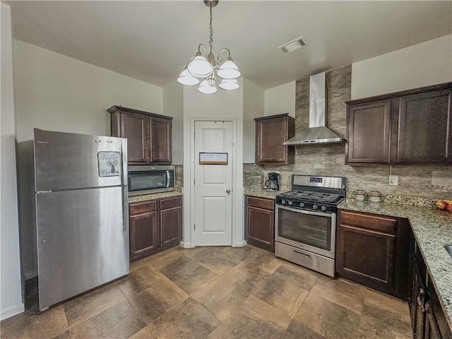 kitchen with wall chimney exhaust hood, light stone counters, decorative light fixtures, stainless steel appliances, and backsplash