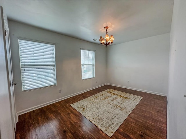 unfurnished room featuring a notable chandelier and dark wood-type flooring