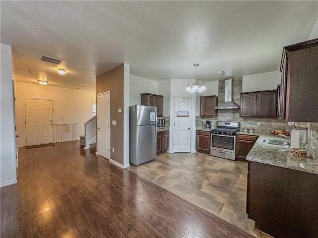 kitchen with backsplash, stainless steel appliances, light stone countertops, dark brown cabinets, and wall chimney range hood