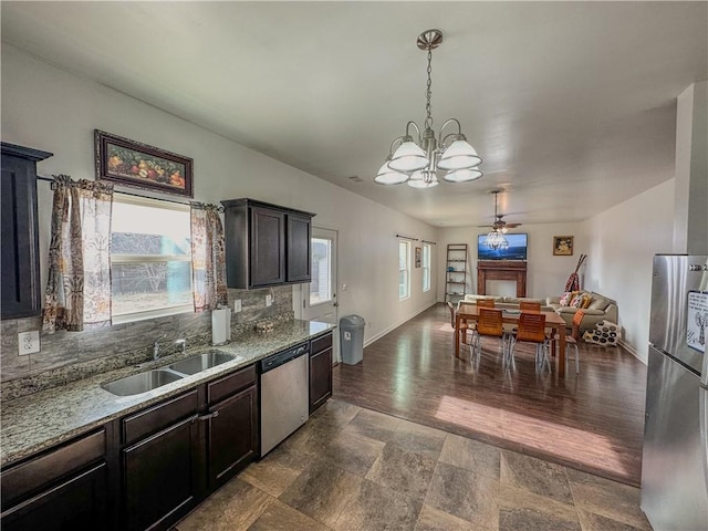 kitchen with sink, hanging light fixtures, stainless steel appliances, light stone countertops, and dark brown cabinets