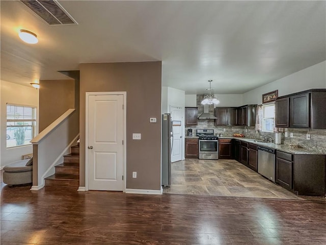 kitchen featuring tasteful backsplash, dark brown cabinets, hanging light fixtures, stainless steel appliances, and wall chimney range hood