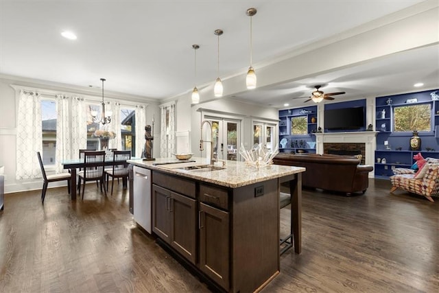 kitchen with light stone countertops, stainless steel dishwasher, pendant lighting, an island with sink, and sink