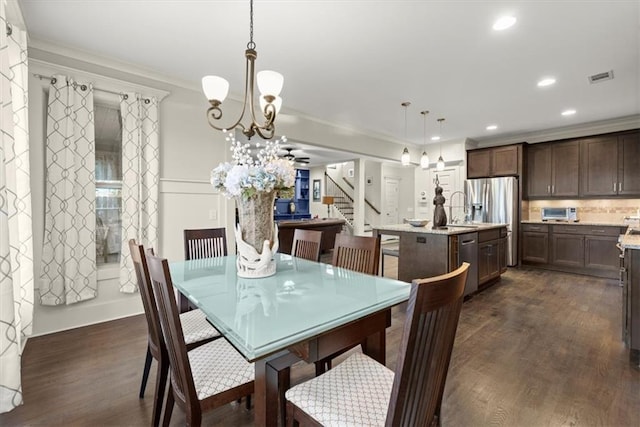 dining area with sink, crown molding, a notable chandelier, and dark wood-type flooring