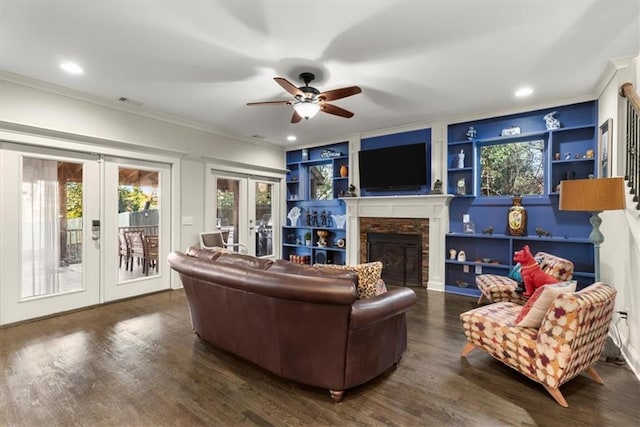 living room featuring french doors, built in shelves, crown molding, a fireplace, and ceiling fan