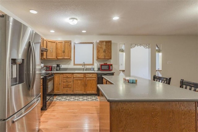 kitchen with light hardwood / wood-style flooring, a textured ceiling, a center island, black appliances, and sink