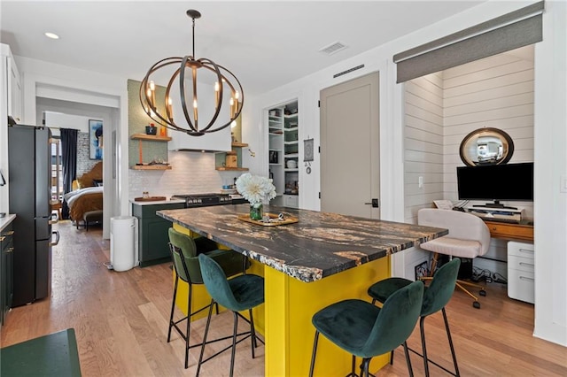 kitchen featuring visible vents, open shelves, freestanding refrigerator, a kitchen bar, and light wood finished floors