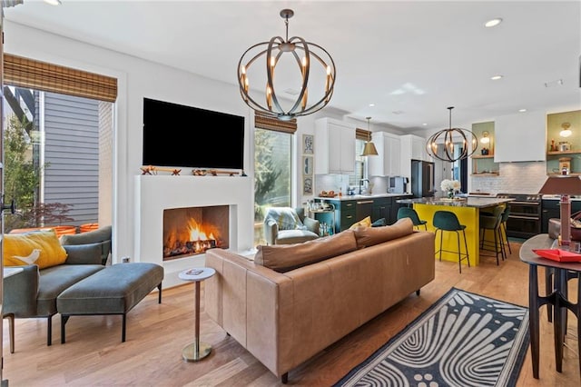 living area featuring a chandelier, recessed lighting, light wood finished floors, and a warm lit fireplace
