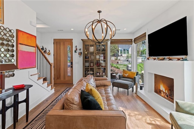 living room featuring an inviting chandelier, a warm lit fireplace, recessed lighting, stairway, and wood finished floors