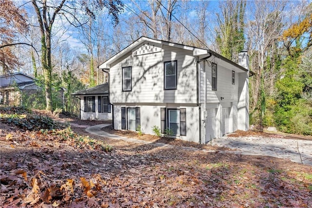 rear view of property featuring a garage, concrete driveway, brick siding, and a chimney