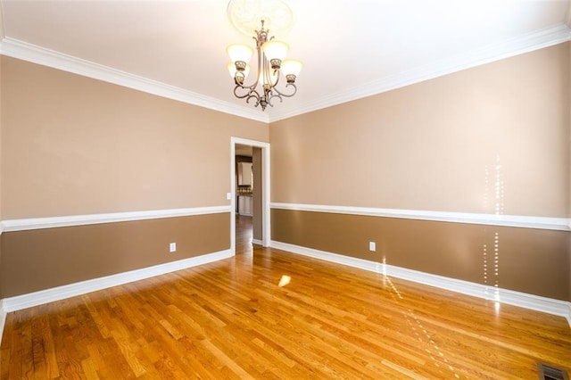 empty room featuring ornamental molding, a notable chandelier, and hardwood / wood-style floors