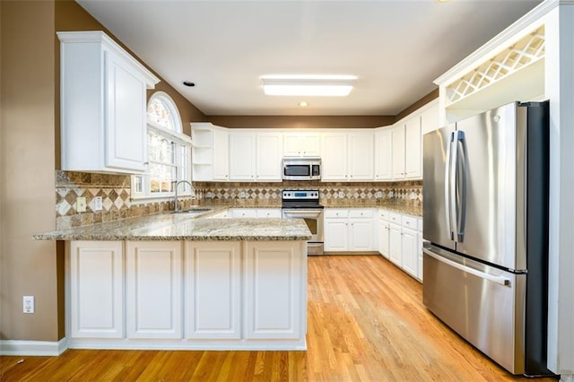 kitchen with kitchen peninsula, appliances with stainless steel finishes, white cabinets, and sink