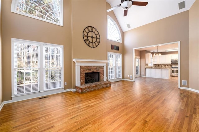 unfurnished living room with a brick fireplace, ceiling fan with notable chandelier, light hardwood / wood-style flooring, and high vaulted ceiling