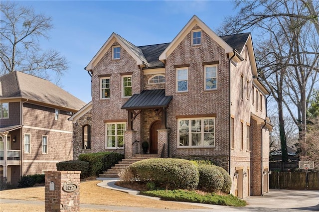 view of front of home featuring a standing seam roof, brick siding, metal roof, and fence