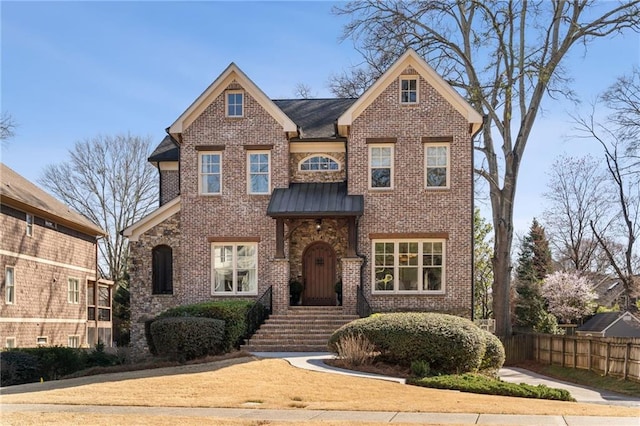 traditional home featuring a standing seam roof, brick siding, fence, and metal roof