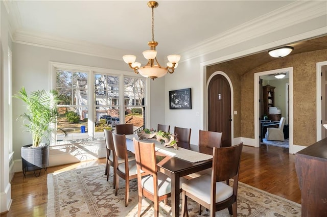 dining area featuring arched walkways, ornamental molding, wood finished floors, and a notable chandelier