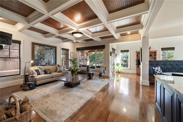 living area featuring coffered ceiling, wood finished floors, baseboards, beamed ceiling, and crown molding